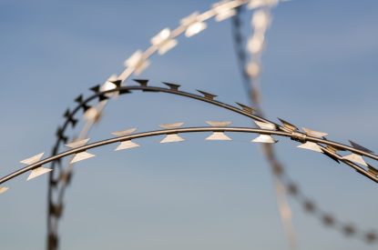 Oberpfaffenhofen, Bavaria / Germany - Sept 28, 2019: Detail / isolated view on sharp, curved razor wire. Blue (sky) background. Used at borders, airports, prison camps, military bases.
